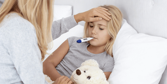 Frau fühlt die Stirn eines kranken Kindes im Bett, das ein digitales Thermometer im Mund hält.