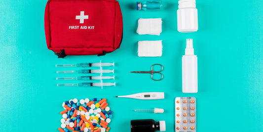 Erste Hilfe Set für unterwegs: rote Tasche mit Pflastern, Binden, Schere und Verbandmaterial auf türkisem Hintergrund