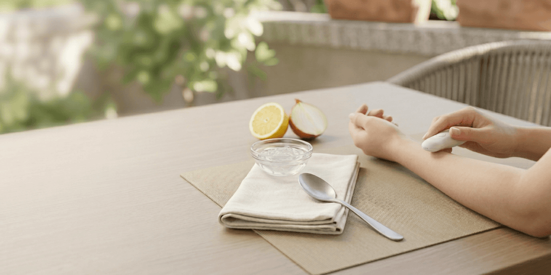 Person hält ein kleines Gerät über dem Unterarm an einem Tisch; daneben Schale mit Wasser, Löffel und halbierte Zitrone.