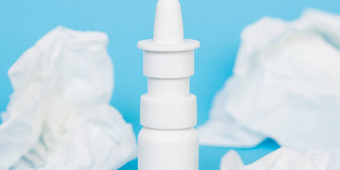Weißes Nasenspray vor blauem Hintergrund mit Papiertaschentüchern, Thema Kochsalzlösung zur Nasenpflege