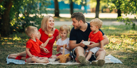 Familie mit drei Kindern beim Sommer-Picknick auf einer Decke im Park, Thema Insektenschutz im Freien