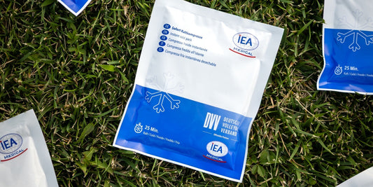 Blau-weiße IEA-Medical-Sofort-Kaltkompressen mit Schneeflocke und DVV-Logo liegen im grünen Gras.