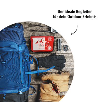 Outdoor-Szene mit Rucksack und Ausrüstung; rote Erste-Hilfe-Tasche liegt daneben; Text: „Der ideale Begleiter für dein Outdoor-Erlebnis“ – Aussage: kompakt für unterwegs beim Wandern/Outdoor.