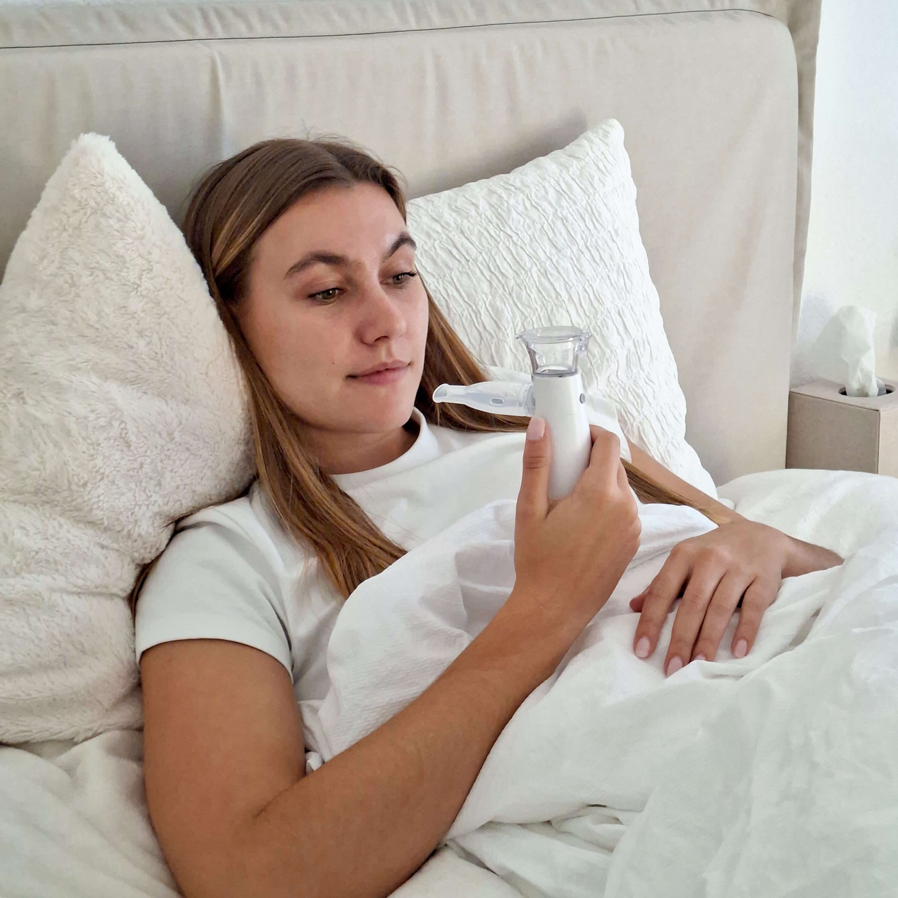 Frau mit Erkältung liegt im Bett und benutzt einen Inhalator mit passendem Mundstück