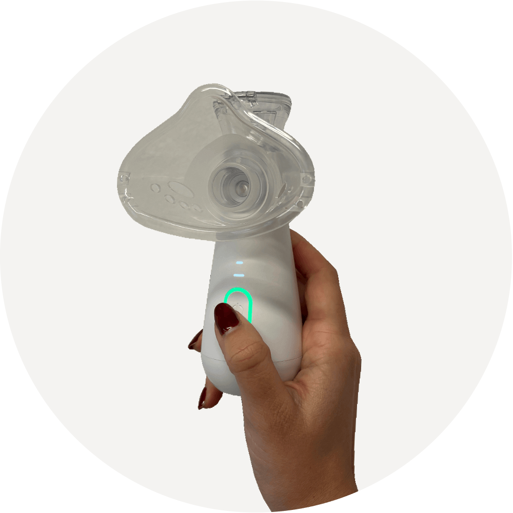 Hand hält Inhaliergerät mit aufgesetzter Maske; leuchtender Einschaltknopf zeigt das Gerät im Betrieb/aktiviert.
