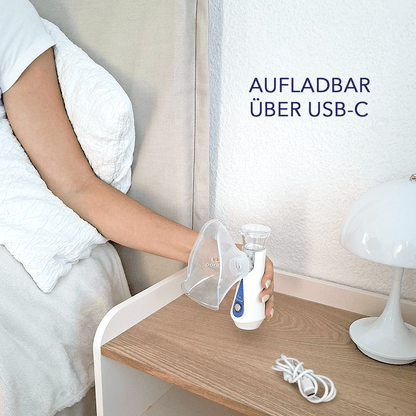 Hand hält den Vernebler auf einem Nachttisch neben Lampe und USB-C-Kabel, Text „Aufladbar über USB-C“.