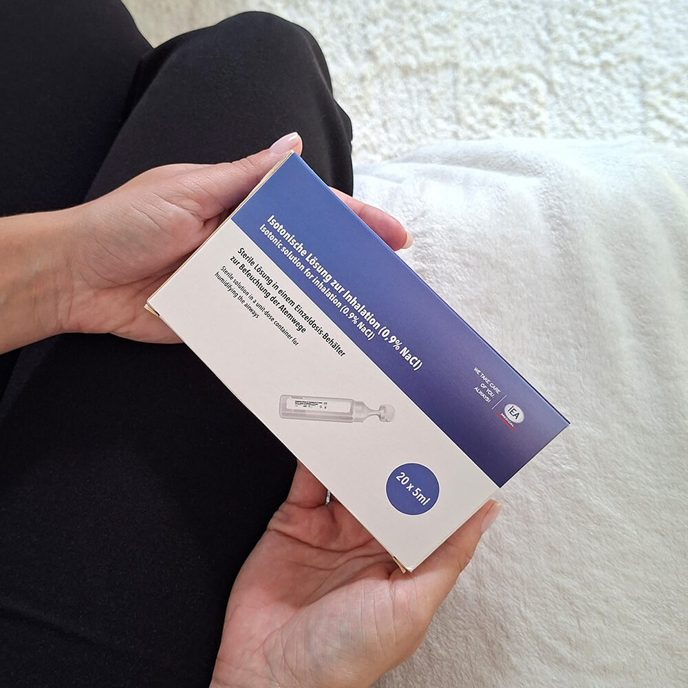 Person hält eine Packung der Kochsalzlösung von IEA Medical in den Händen