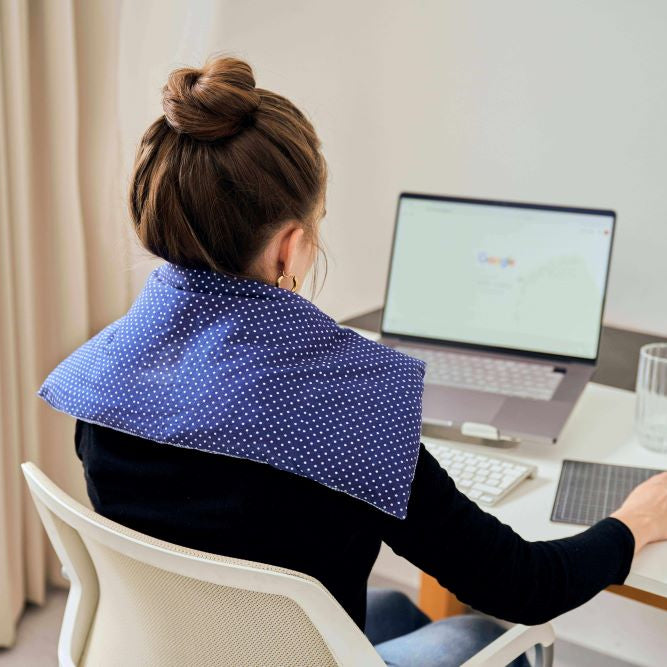 Frau sitzt am Schreibtisch und arbeitet mit Körnerkissen auf dem Nacken