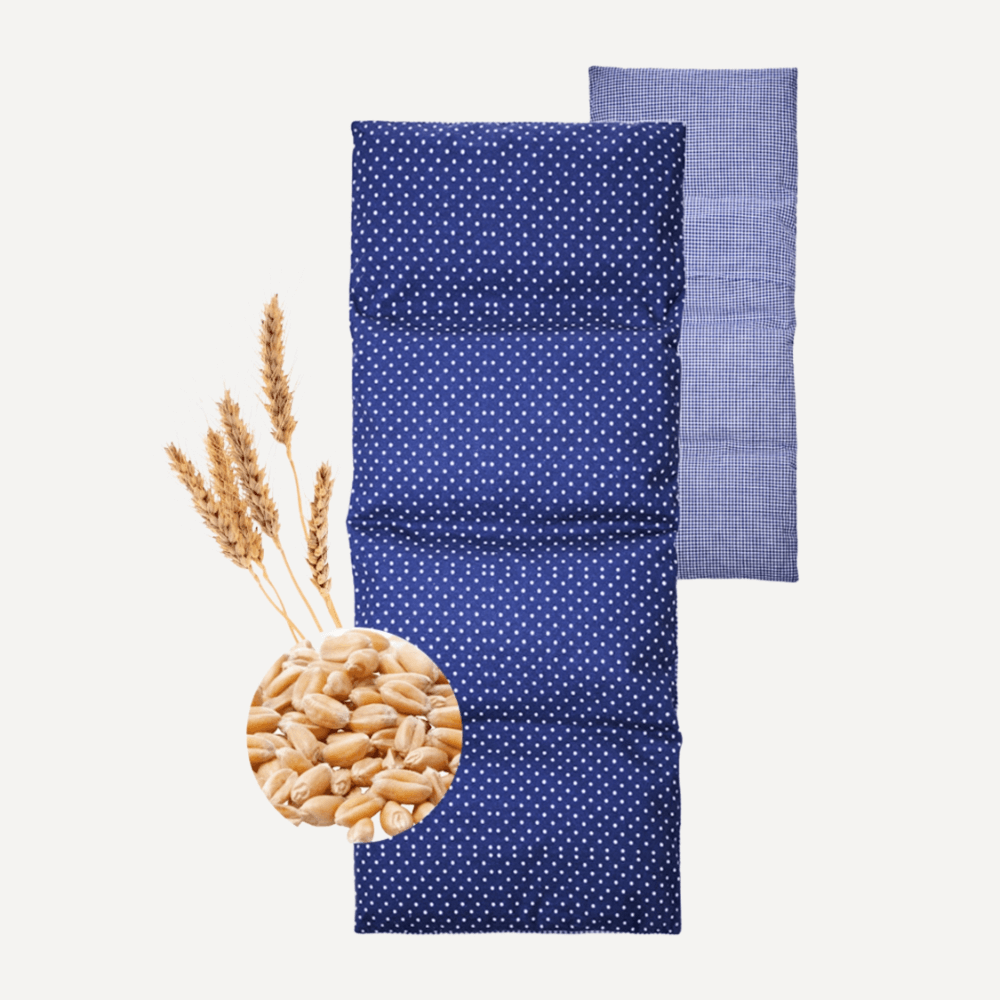 Längliches Körnerkissen mit blauer Punkteseite und blau kariertem Bezug, daneben Weizenähren und Körner.