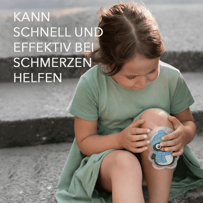 Kind hält pinguinförmige Kompresse ans Knie, Bildtext nennt Einsatz bei Schmerzen.
