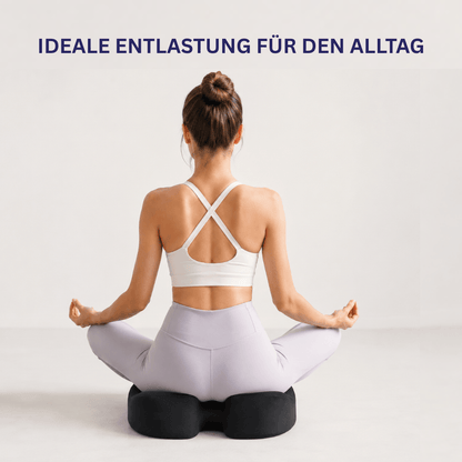 Frau sitzt im Schneidersitz auf schwarzem Sitzkissen am Boden, von hinten, Text Ideale Entlastung für den Alltag.