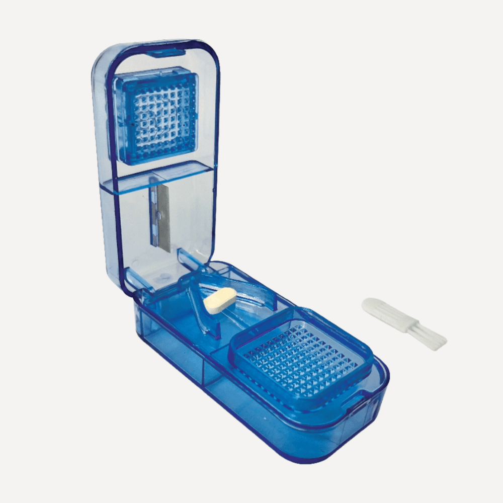 Geöffneter blauer transparenter Tablettenteiler mit weißer Tablette im Fach und kleinem weißen Spachtel daneben.