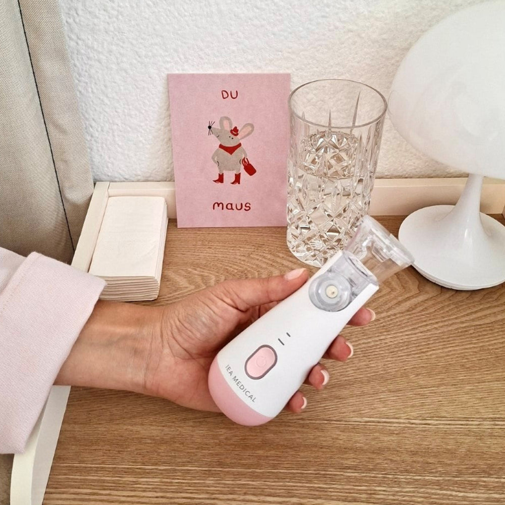 Frau hält pinkes Inhalationsgerät von IEA Medical auf dem Nachttisch