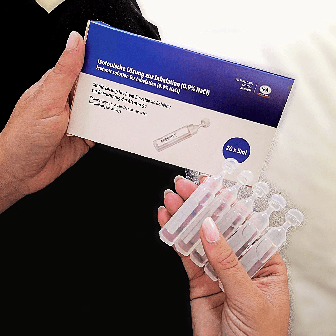 Hände halten IEA Verpackung isotonischer Kochsalzlösung 0,9 % NaCl zur Inhalation, 20 x 5 ml, und aufgefächerte Ampullen.
