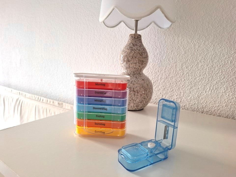 Blauer Tablettenzerteiler und bunte Medikamentenbox von IEA Medical stehen auf dem Regal