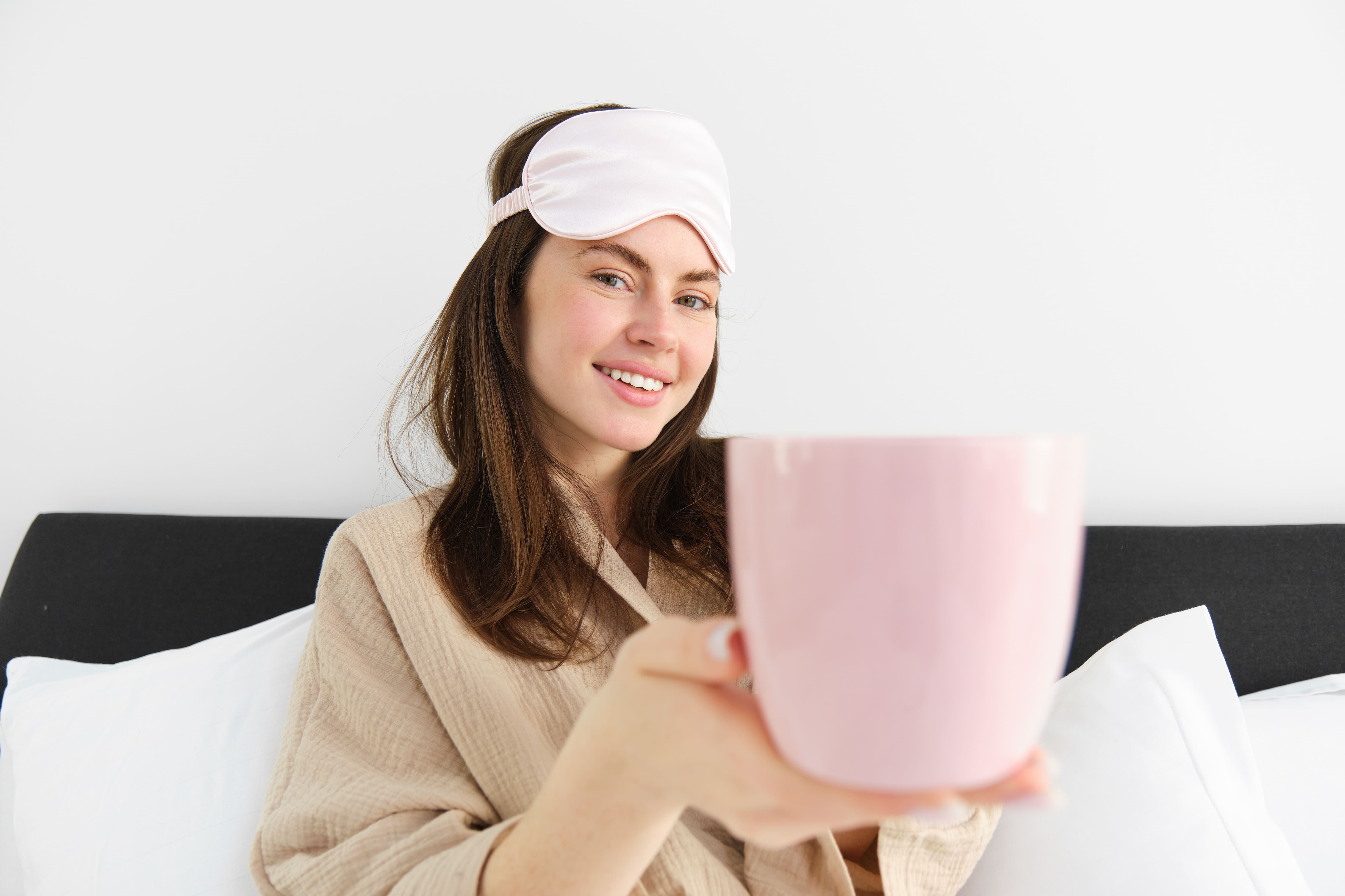 beautiful-smiling-modern-woman-pyjamas-sleeping-mask-offering-cup-tea-coffee-bed